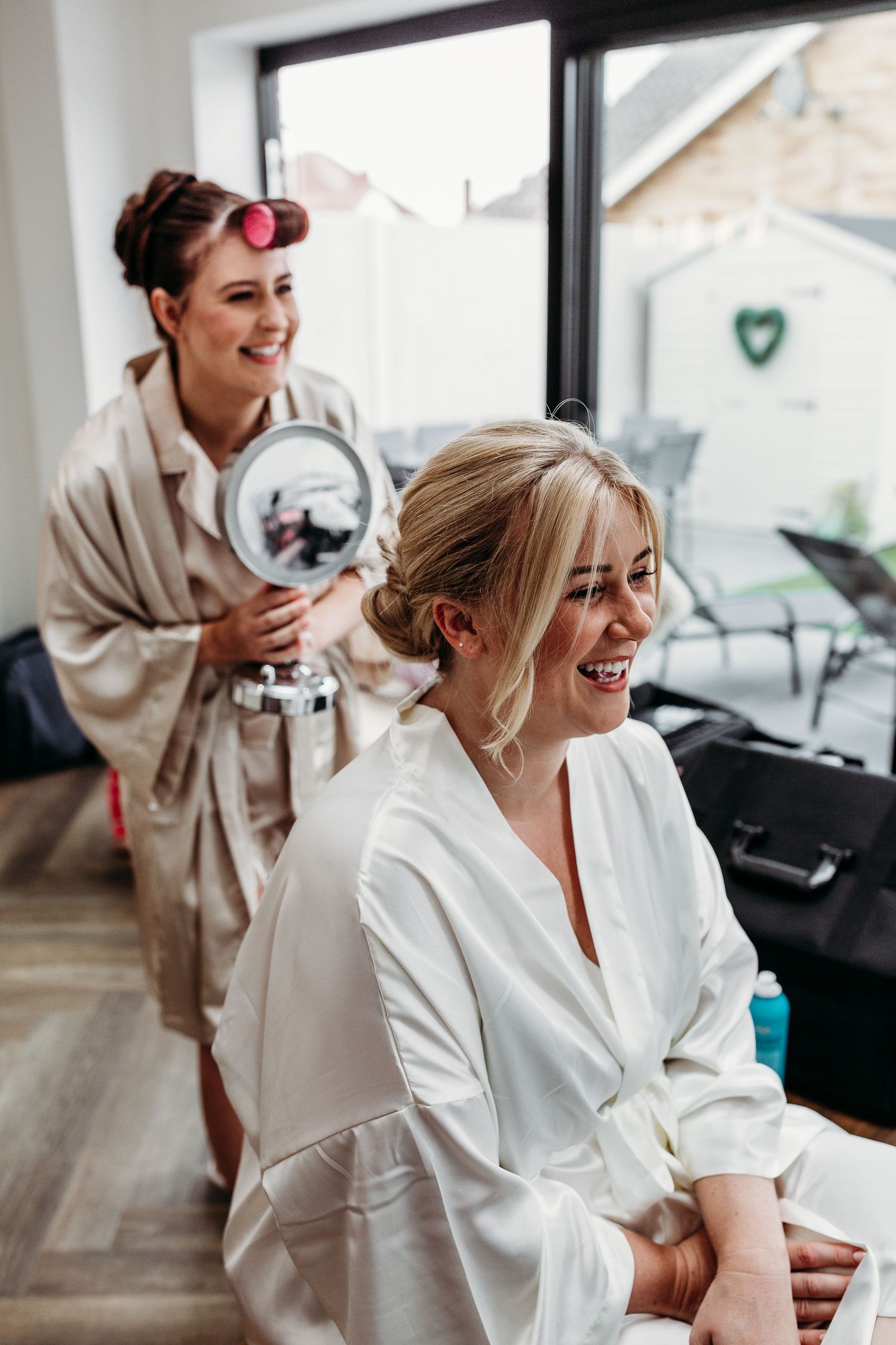 Two people laughing and getting ready in white robes during a special occasion preparation.