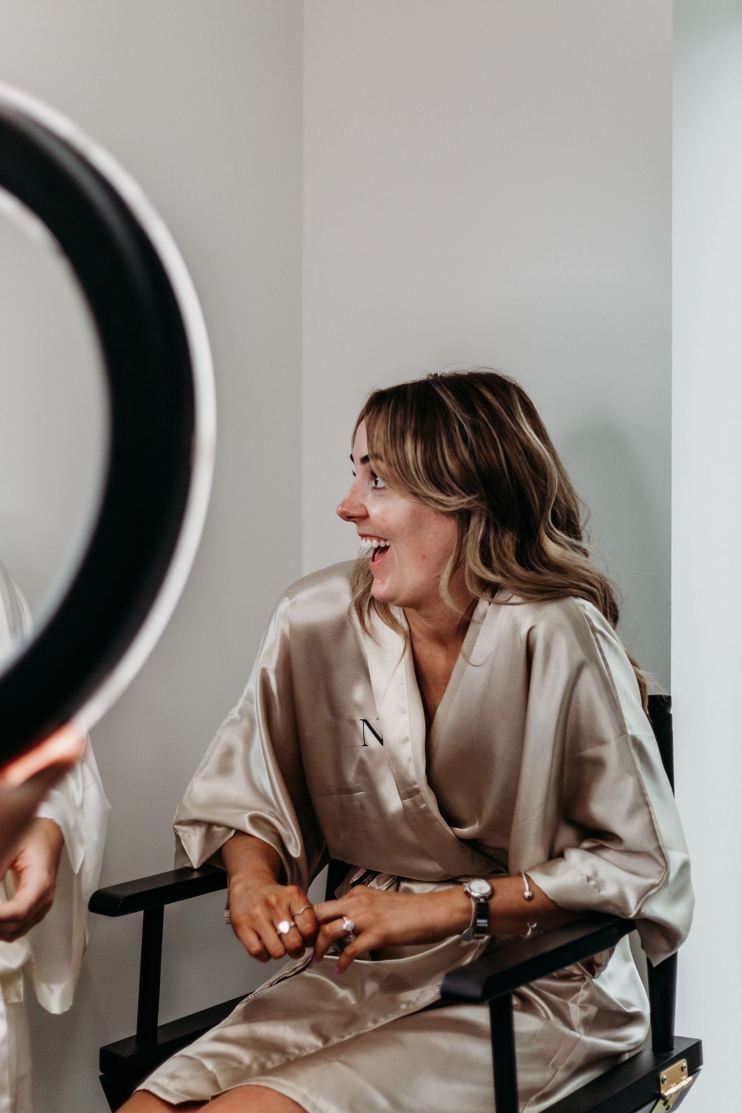 Person in silk robe laughing joyfully while seated during a getting-ready session.