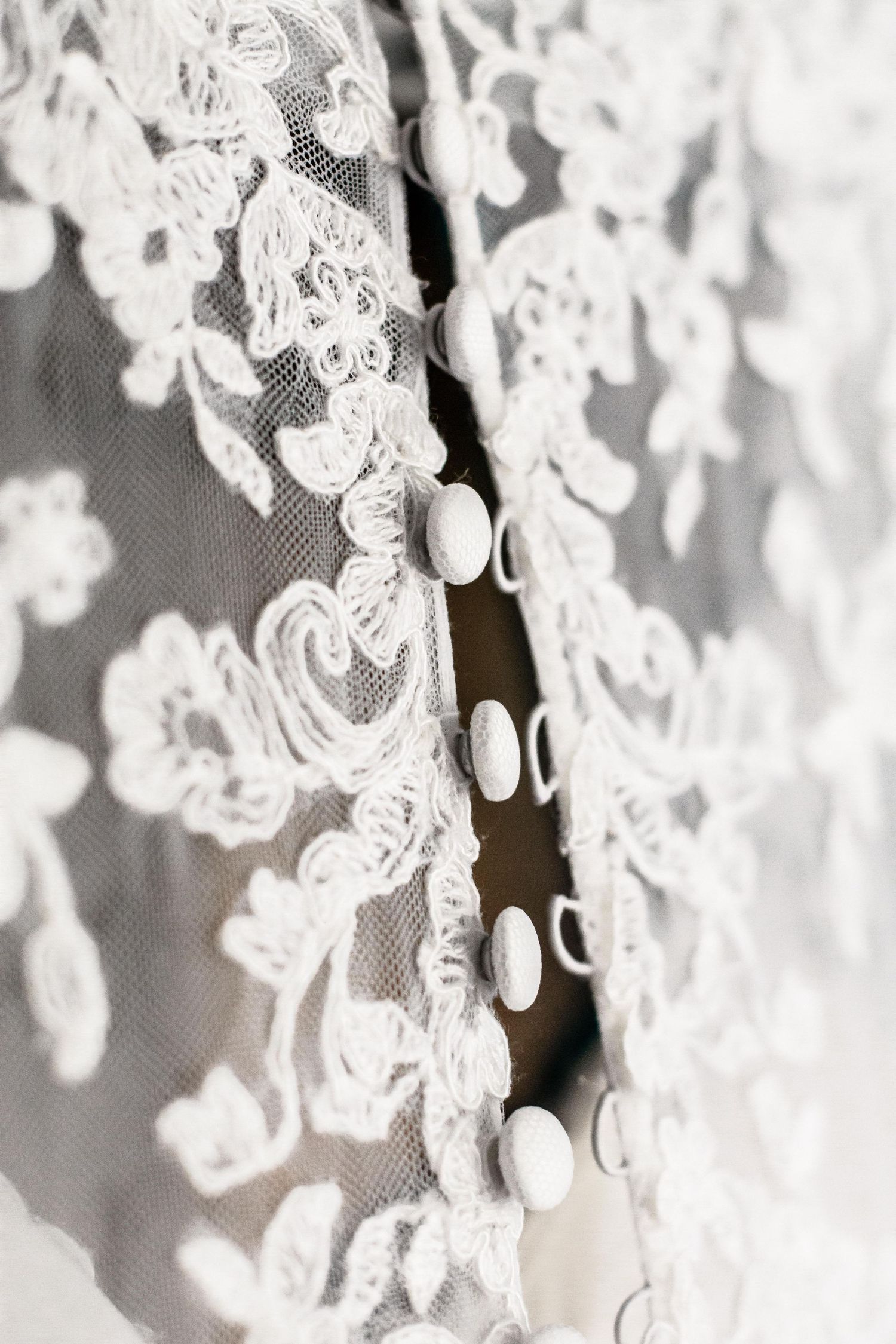 Close-up detail of delicate white lace fabric with floral patterns and button closures.