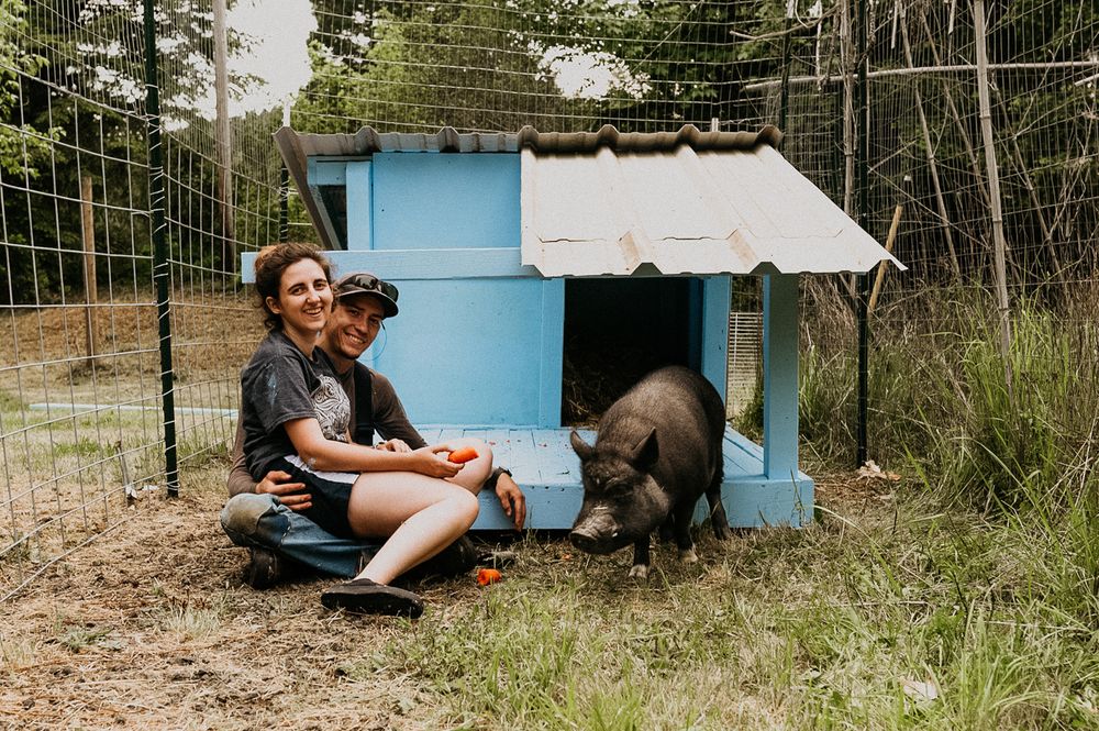 Casual outdoor photoshoot near a vintage blue camper trailer in a wooded setting.