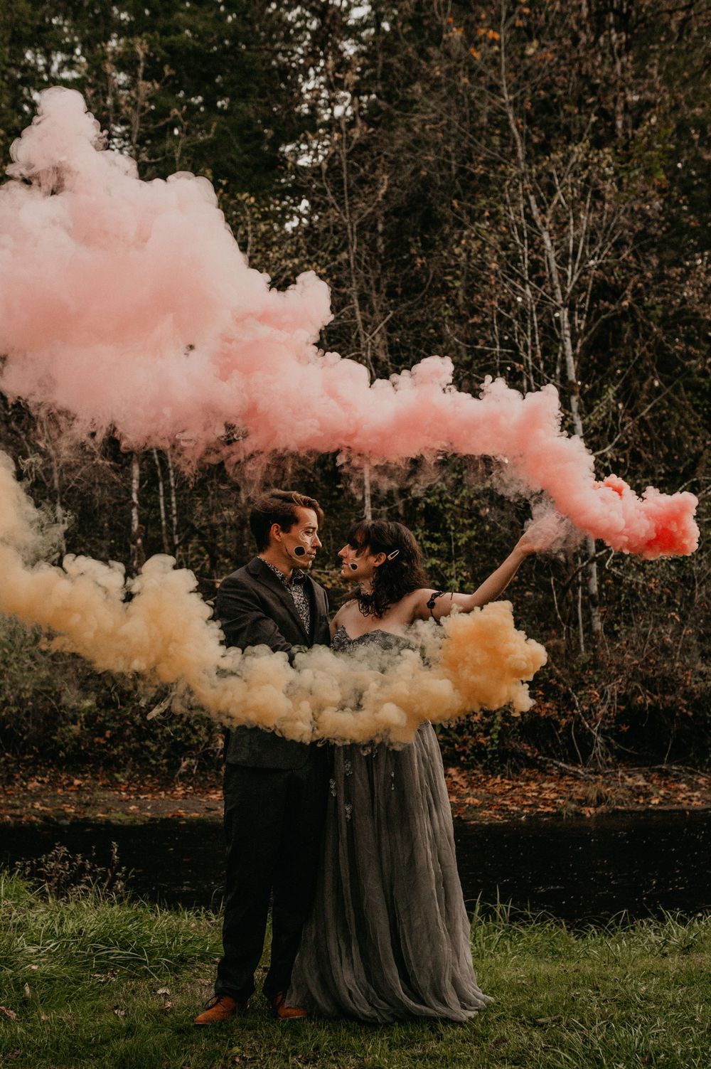 Pink and orange smoke billowing from tree stumps in a grassy field.