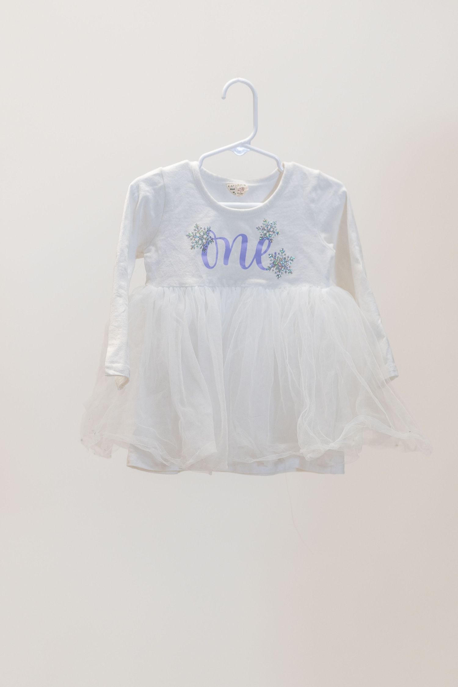 White long sleeve dress with 'one' script text and floral details on a hanger.
