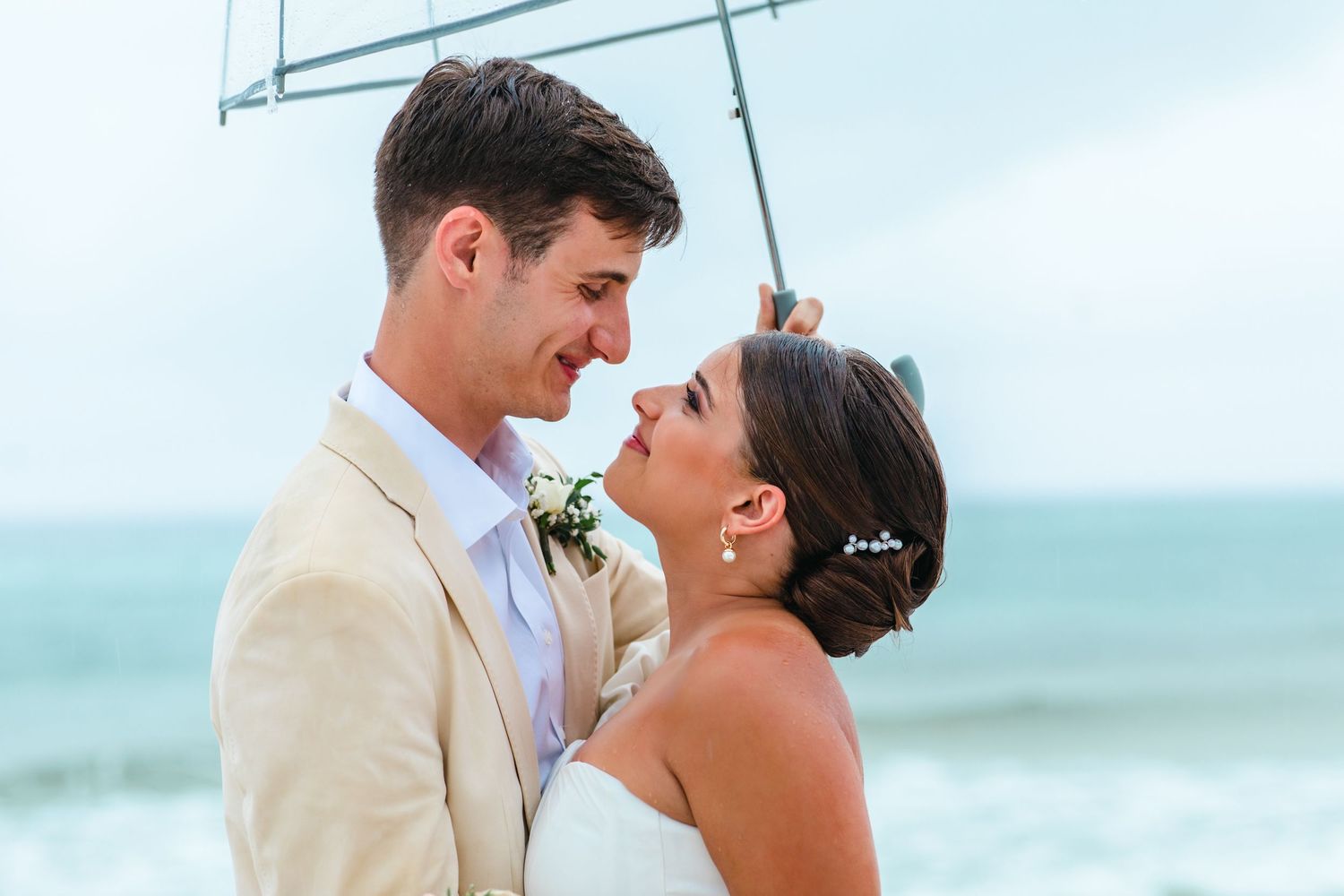 A couple shares a joyful moment by the ocean in beach wedding attire.