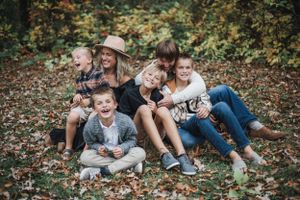 A group lounges together on fall leaves during an outdoor photo session in nature.
