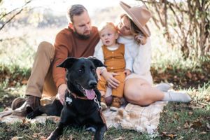 A happy family sits on grass with their black dog on an autumn day in nature.