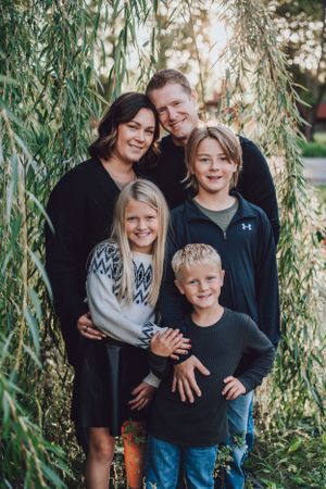 Family group posed together under drooping willow tree branches in natural outdoor setting.