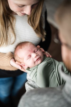 A sleeping newborn wrapped in mint green is cradled gently by caretakers.