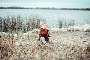 A small child in a red sweater plays joyfully near a winter lake with dried reeds.