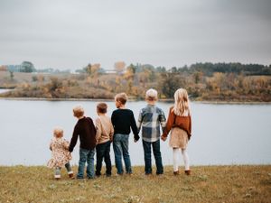 Group sitting together on grassy shoreline overlooking serene autumn lake landscape.