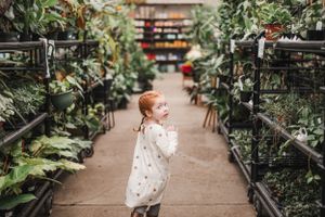 A small child explores a lush greenhouse filled with plants and greenery.