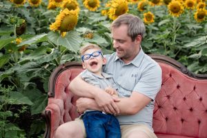 Candid family moments captured on a vintage couch in a blooming sunflower field.