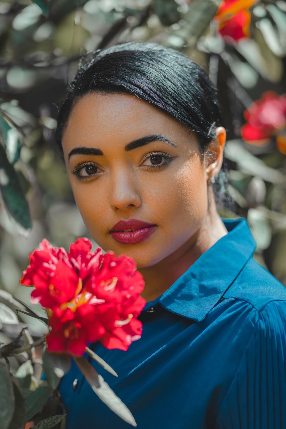 Portrait in blue against vibrant red flowers in natural outdoor setting.