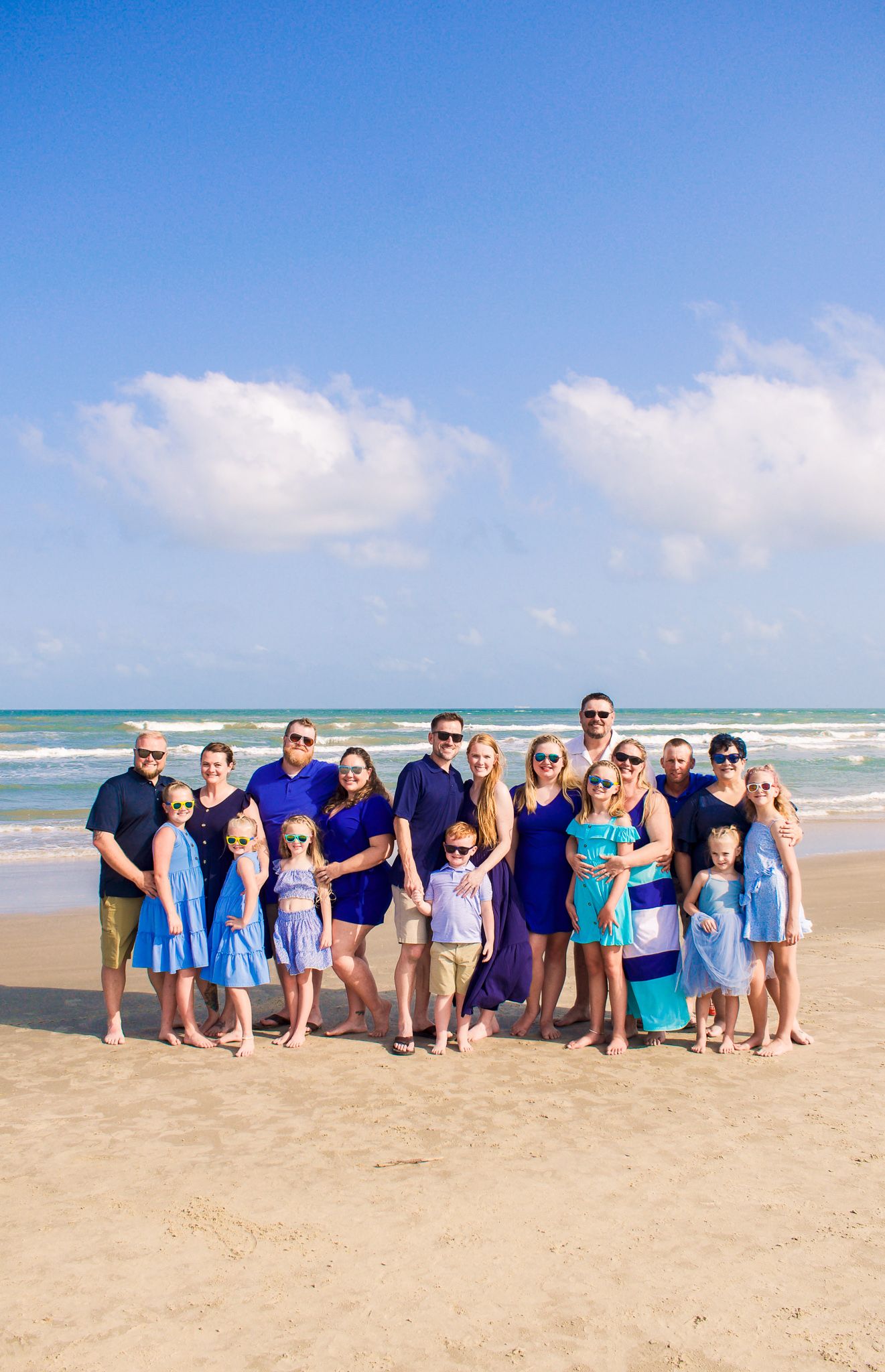 Large family group photo on a sunny beach wearing coordinated blue and white outfits.
