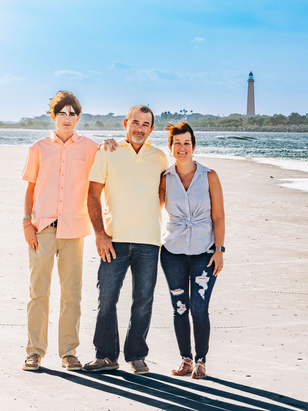 Three people standing on beach with lighthouse visible in background.