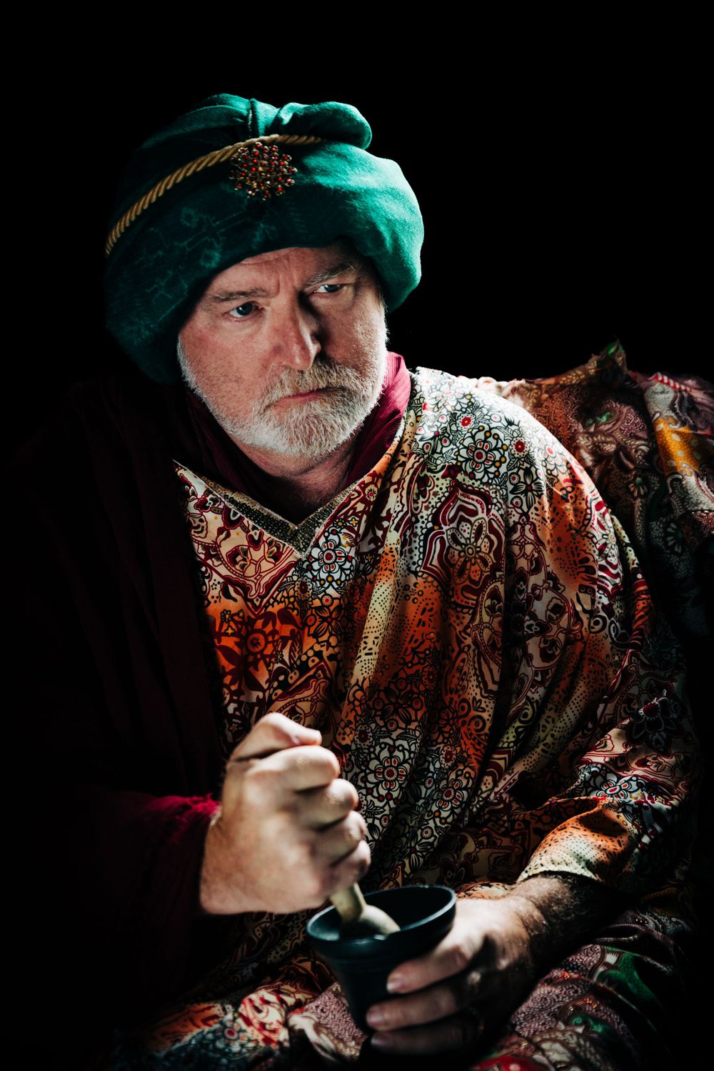 Person wearing traditional Middle Eastern attire with turquoise turban in dramatic lighting.