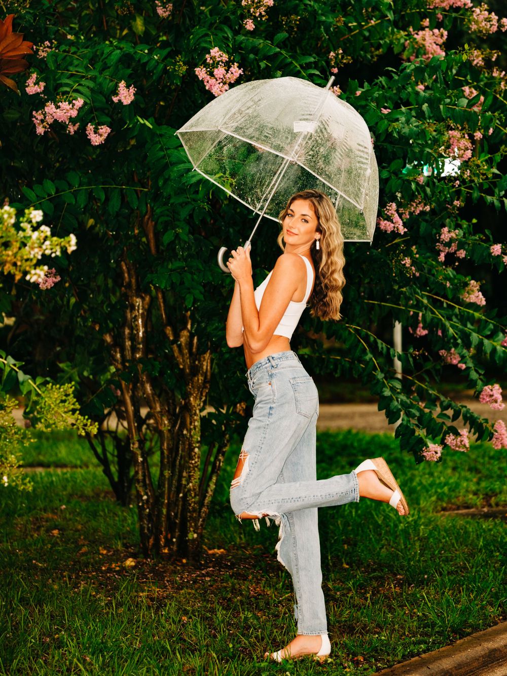Playful pose with clear umbrella against flowering garden background.