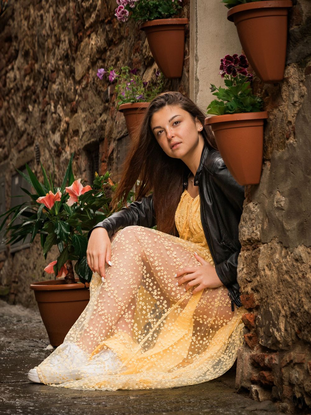 Portrait among flower pots showing yellow lace dress and leather jacket styling.