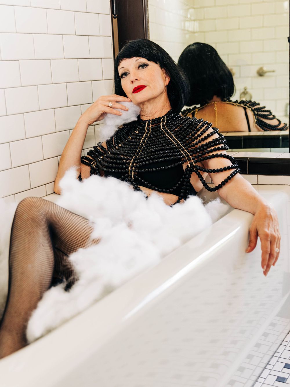 Glamorous bathtub scene with dramatic lighting and white bubbles against subway tile backdrop.