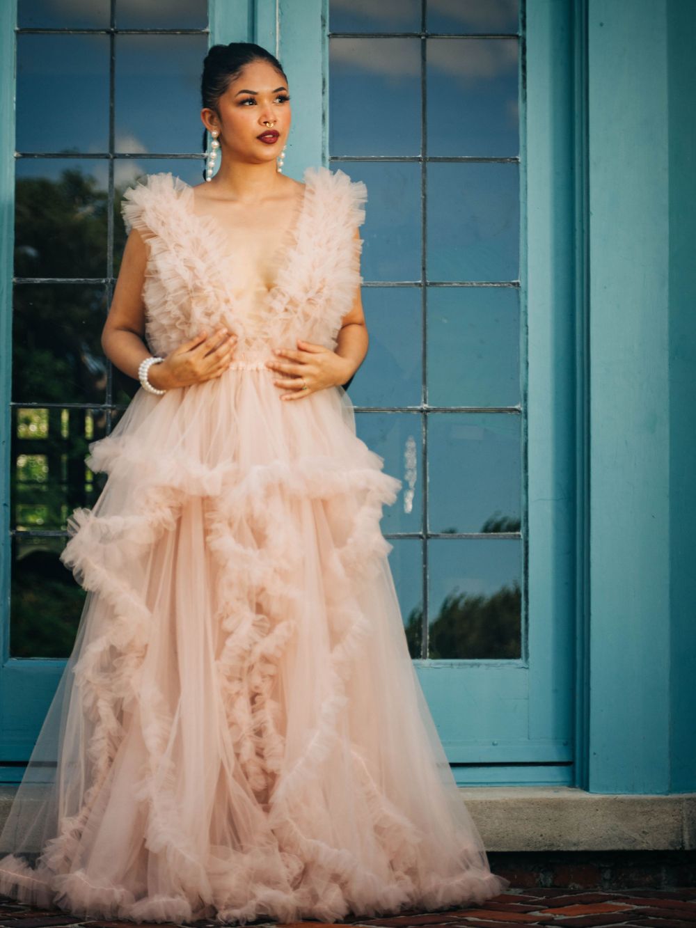 Dramatic fashion photo of model in flowing blush tulle gown against turquoise doors.