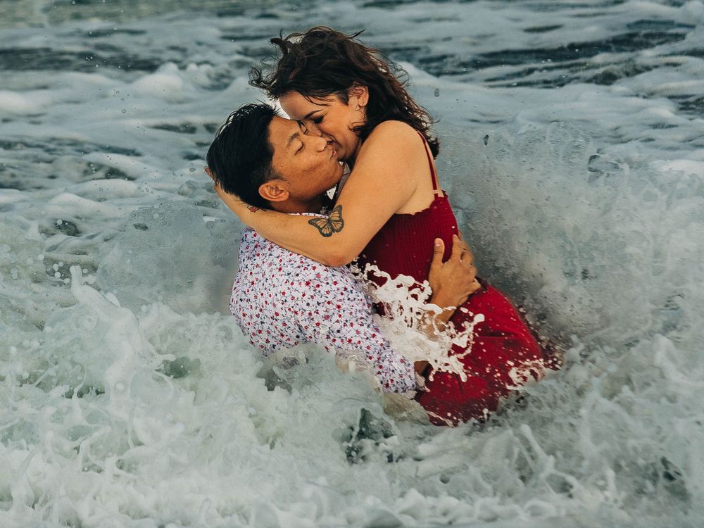 A couple embraces passionately in crashing ocean waves during a romantic beach photoshoot.