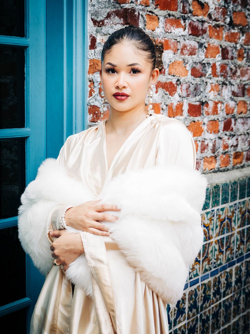 Elegant bridal portrait against brick wall with model wearing white fur wrap and silk dress.