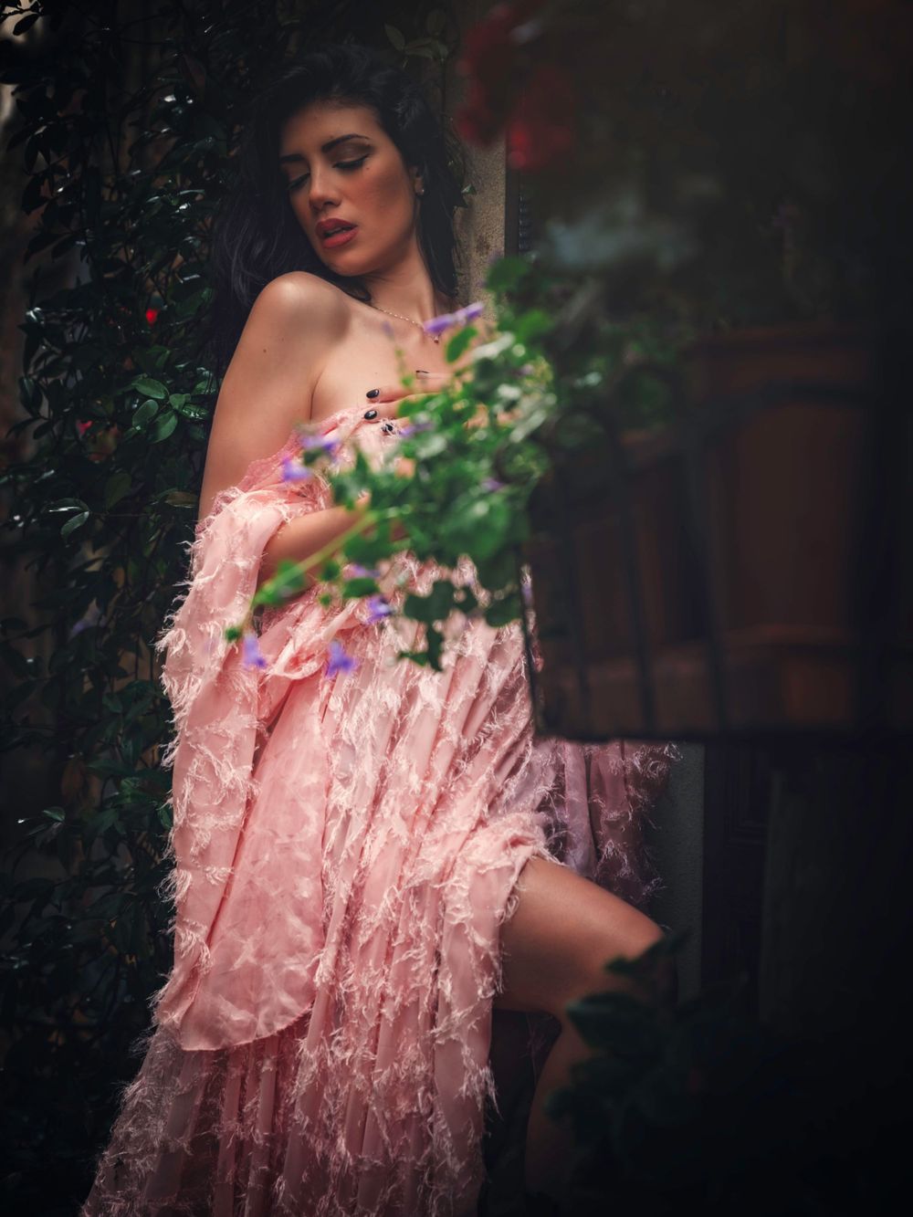 Dreamy fashion photograph featuring pink textured gown against dark garden backdrop.