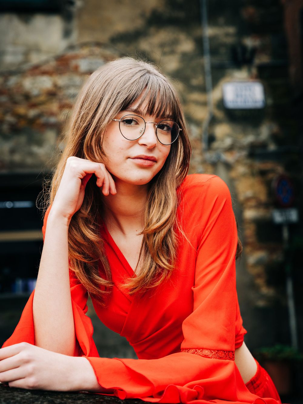 Portrait of woman in bright red outfit against rustic stone wall background.
