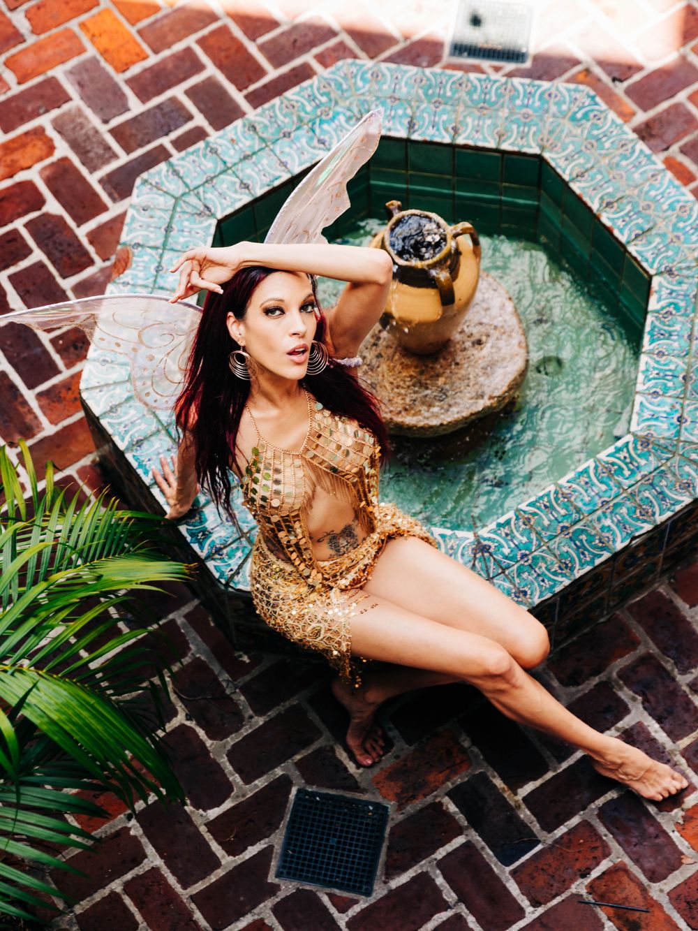 Aerial view of a person in a gold sequined outfit posing by an octagonal tiled fountain.