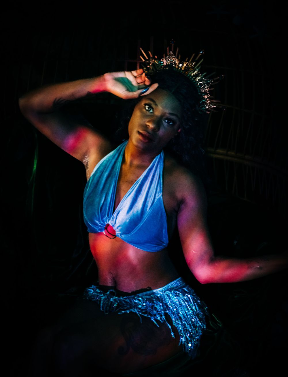 A dancer in blue performing under dramatic colorful lighting against a dark background.