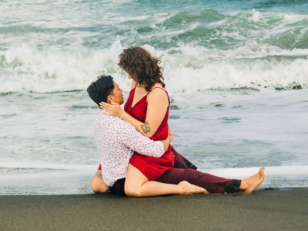 Couple in red and white outfits sharing intimate moment by ocean waves.