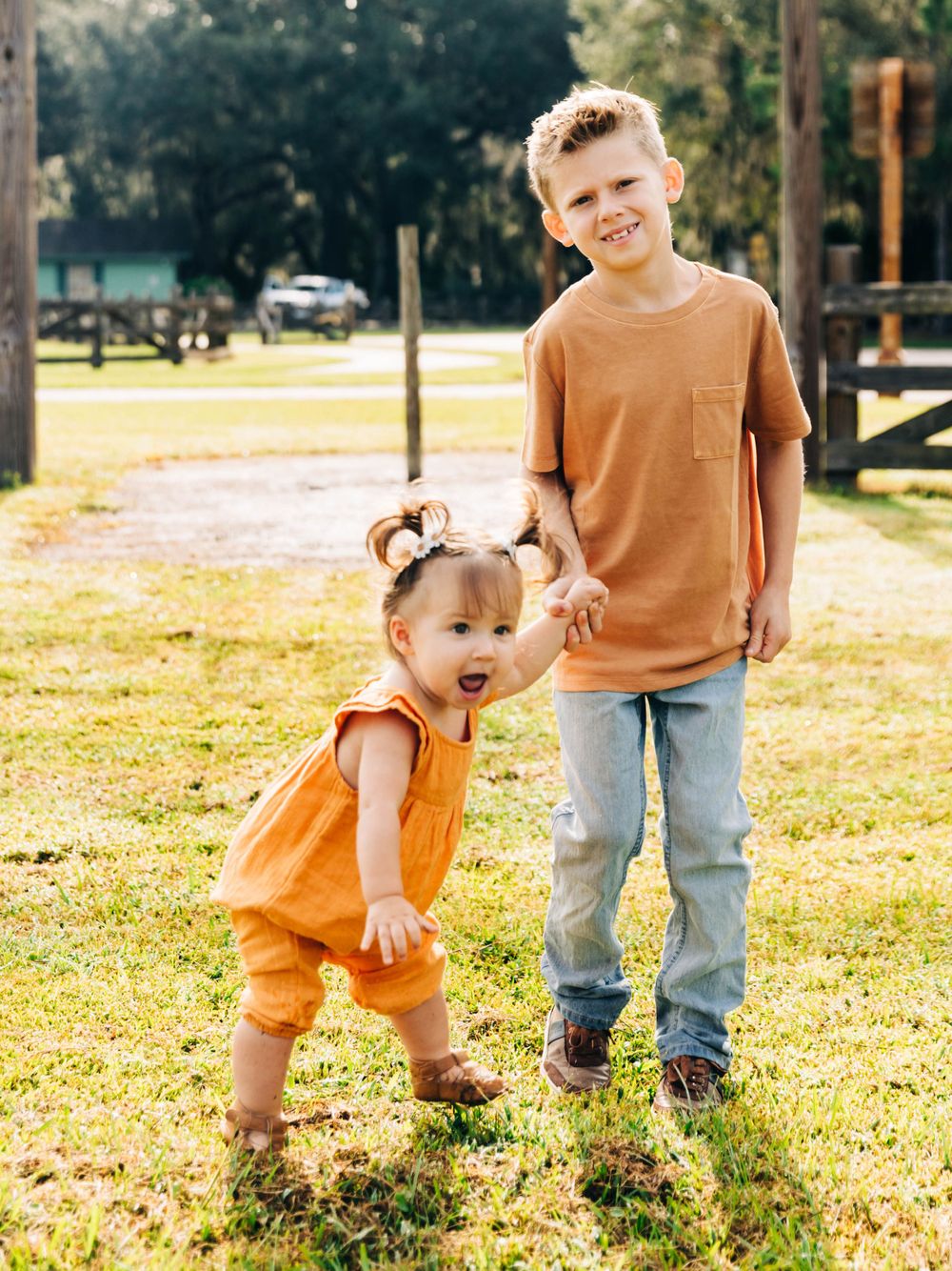 Two children in orange outfits playing together on grass in a park.