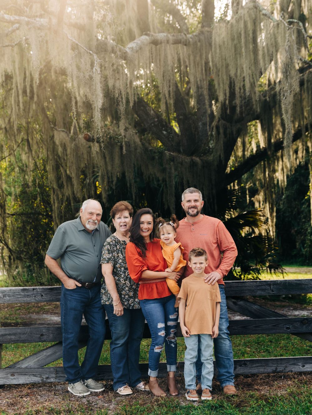 Multi-generational family poses together under Spanish moss covered trees in a park.