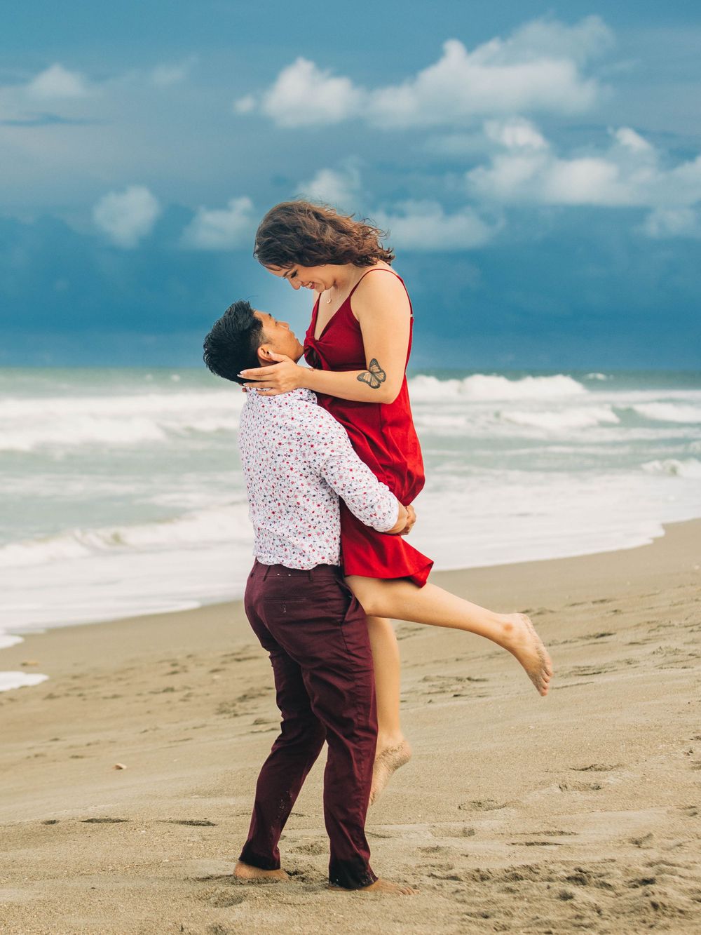 Couple in coordinating red and white outfits embracing on sandy beach.