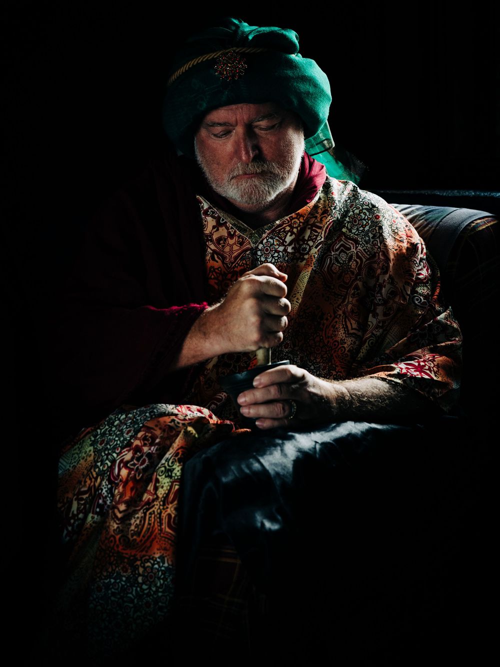 A dramatic portrait of someone in ornate Eastern-style robes and turban against a dark background.