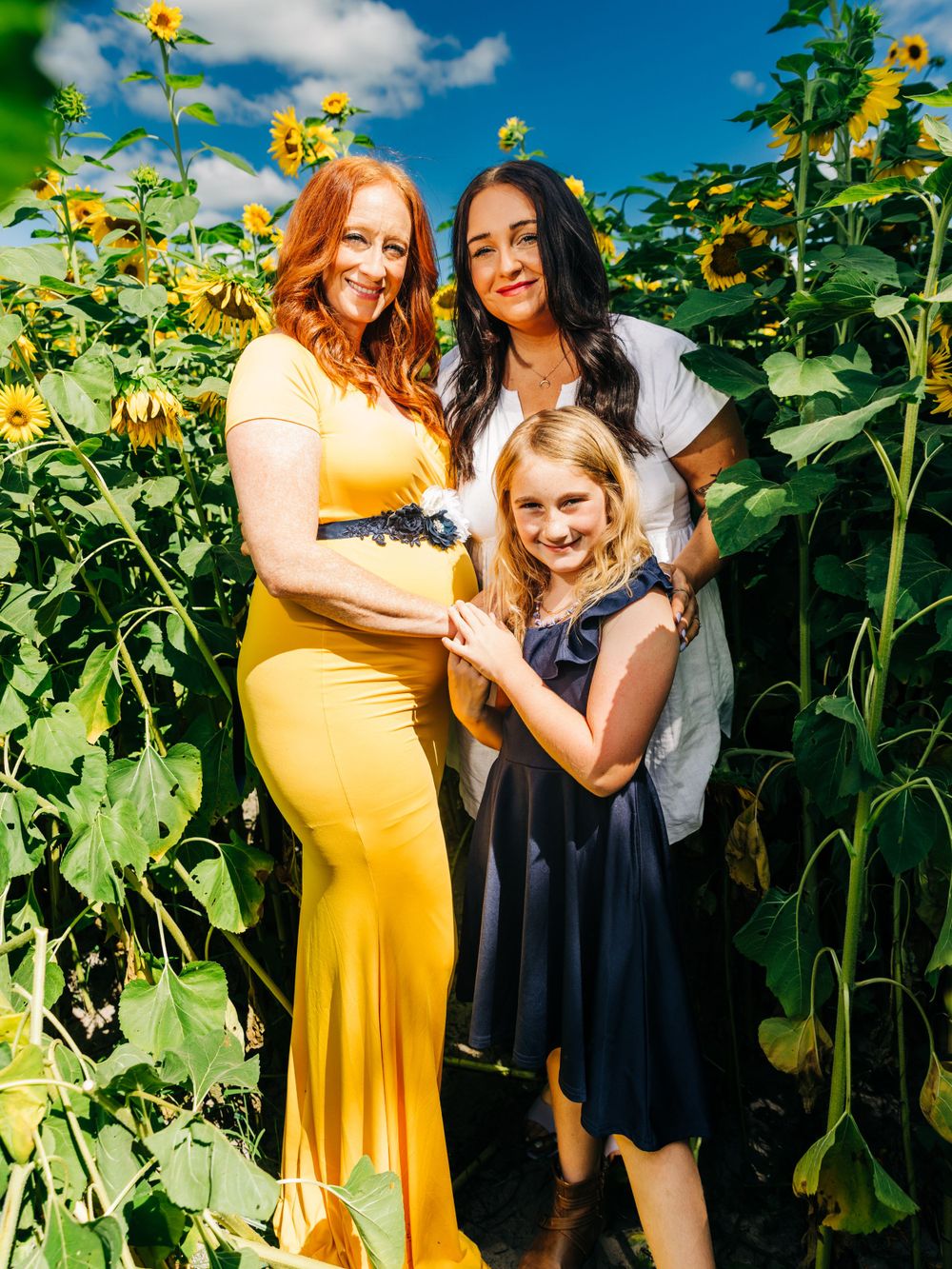 Three people pose together in a sunflower field on a bright summer day.