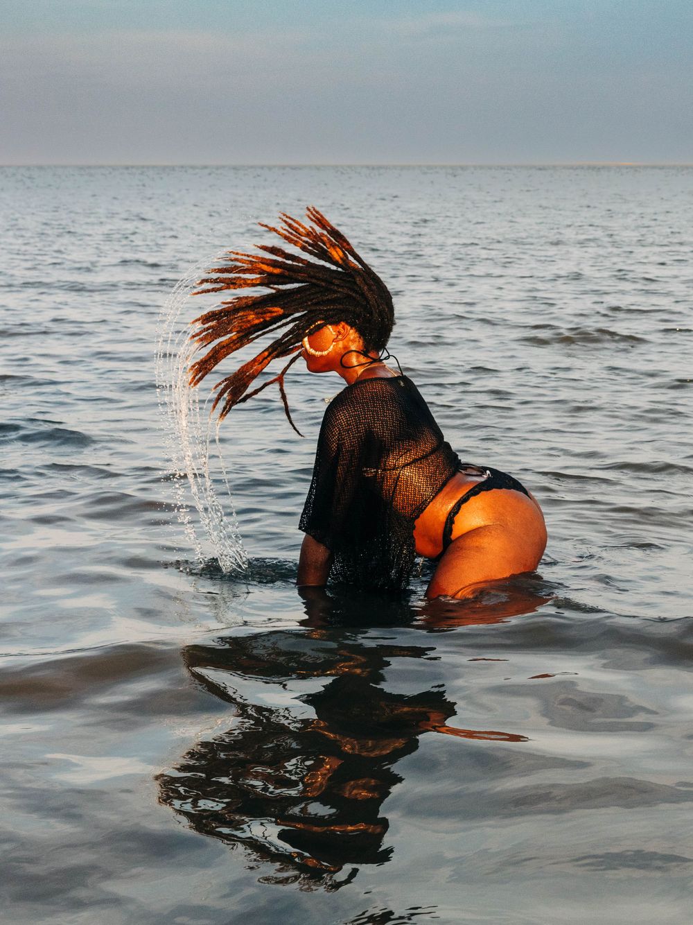 A dramatic water portrait showing hair flipping motion against an ocean backdrop.