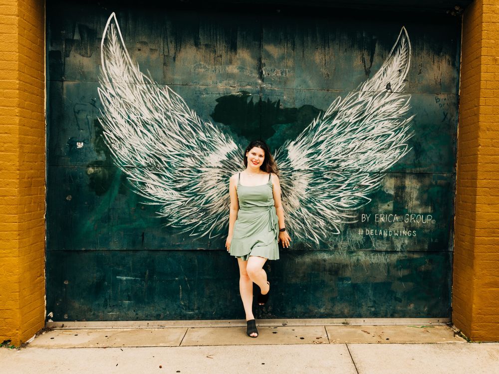 Street art mural featuring large white angel wings painted on a green wall creates an interactive photo opportunity.