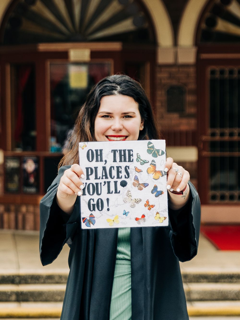 A sign reading 'Oh the places you'll go!' held up in front of a historic building entrance.