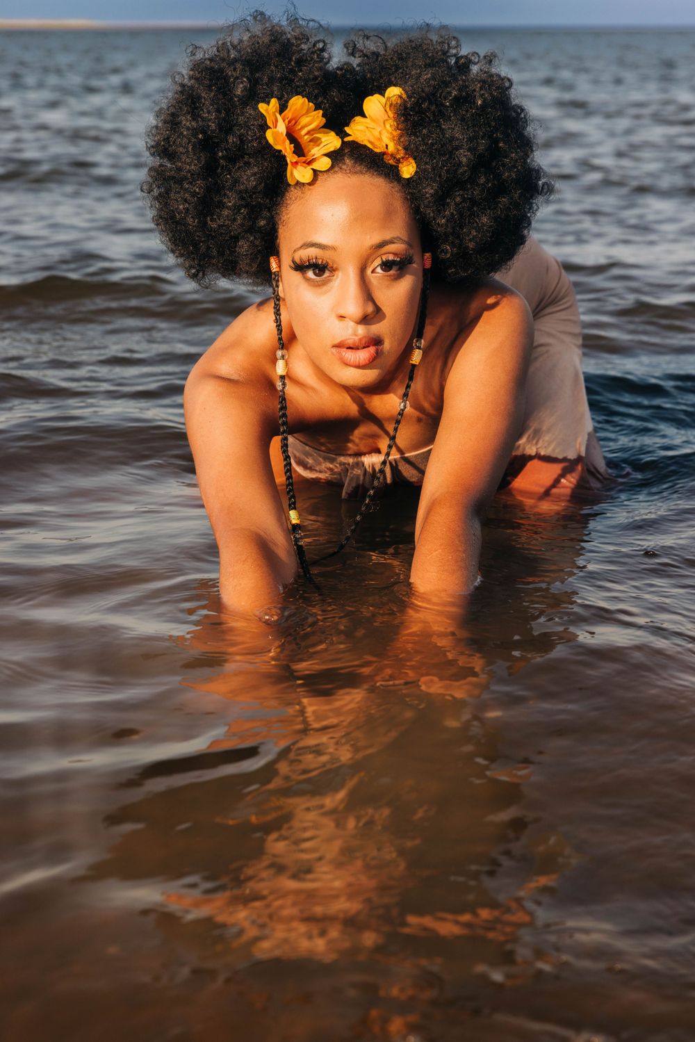 A model in water wearing orange hair accessories during a beach photoshoot.