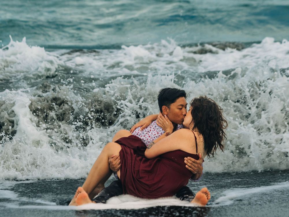 Two people share an intimate moment while laying in rolling ocean waves.