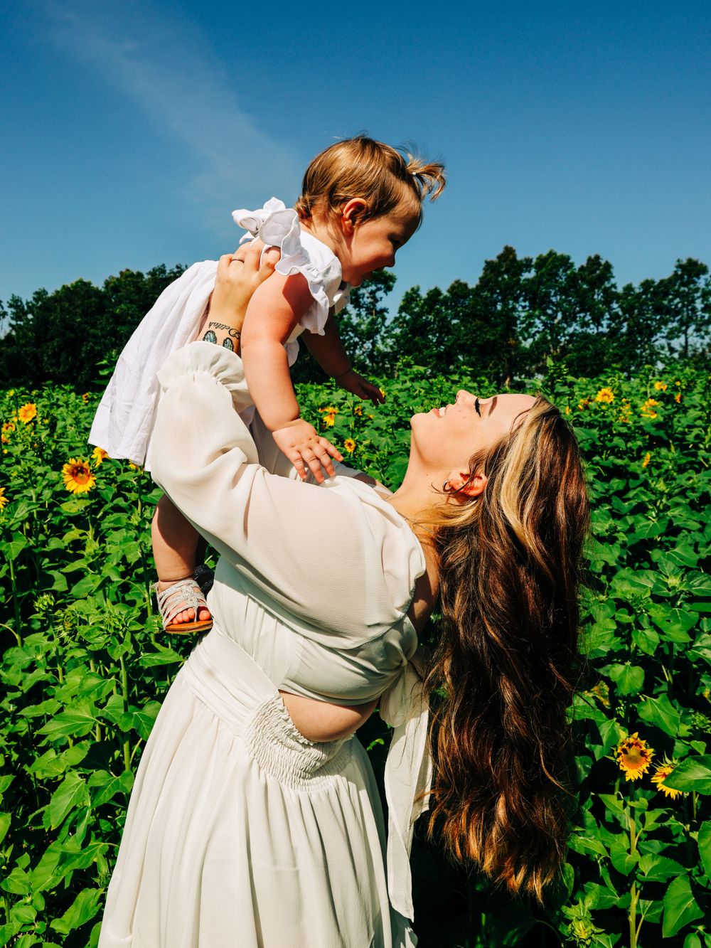 A joyful moment captured in a sunflower field with golden blooms and blue sky.
