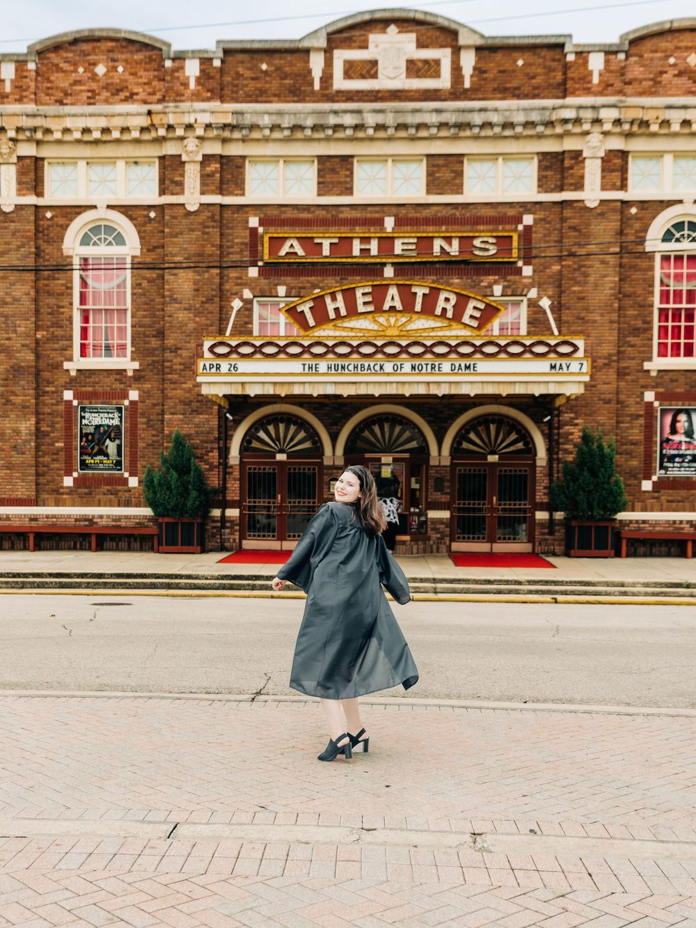 A figure twirls in a flowing dress outside the historic Athens Theatre with its vintage brick facade.