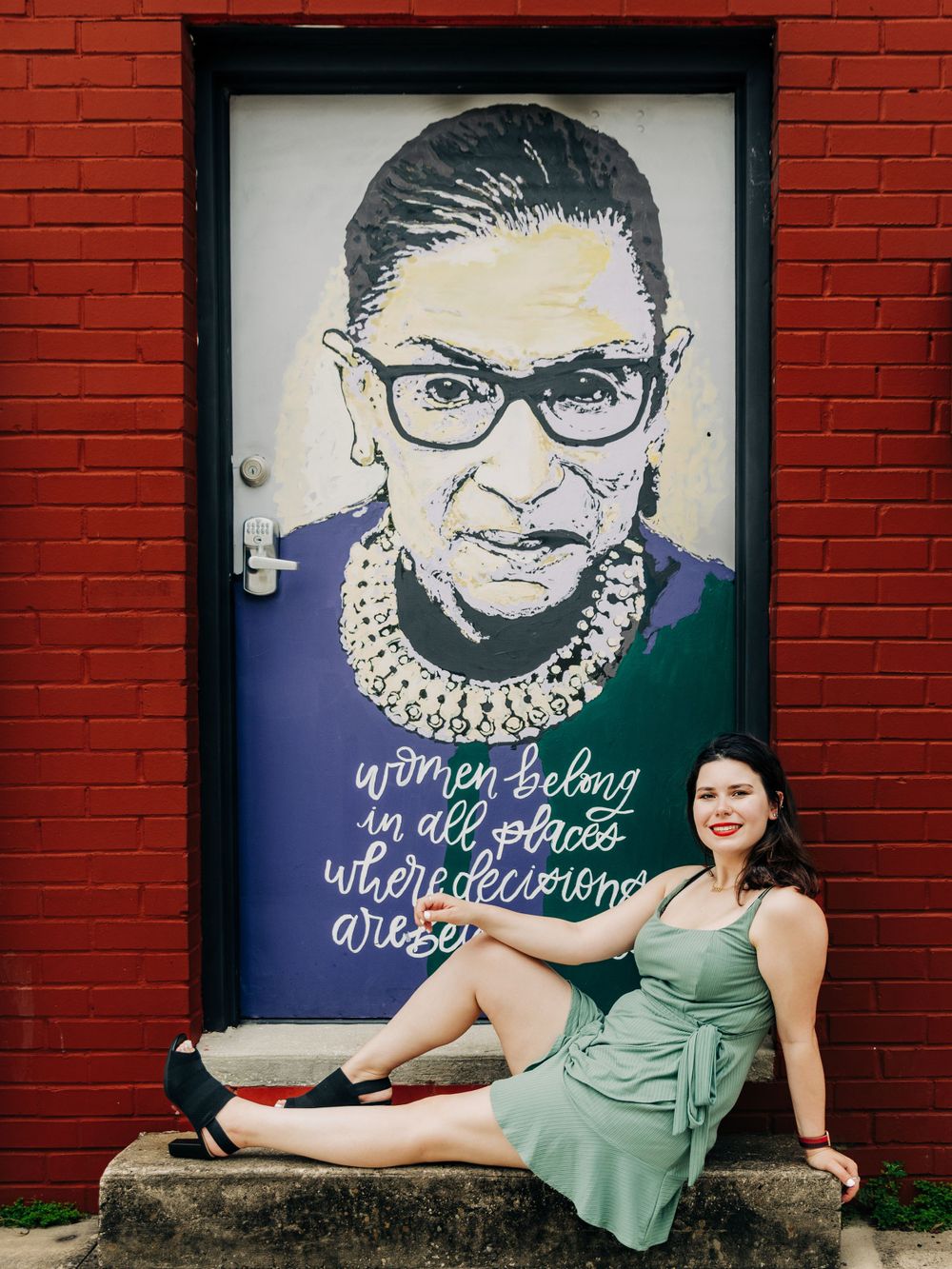 A green dress portrait posed next to a Ruth Bader Ginsburg mural on a red brick wall.