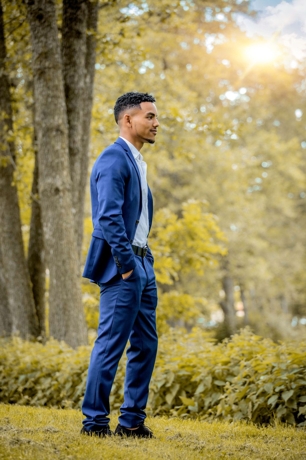 Person in navy suit stands thoughtfully in golden autumn park setting.