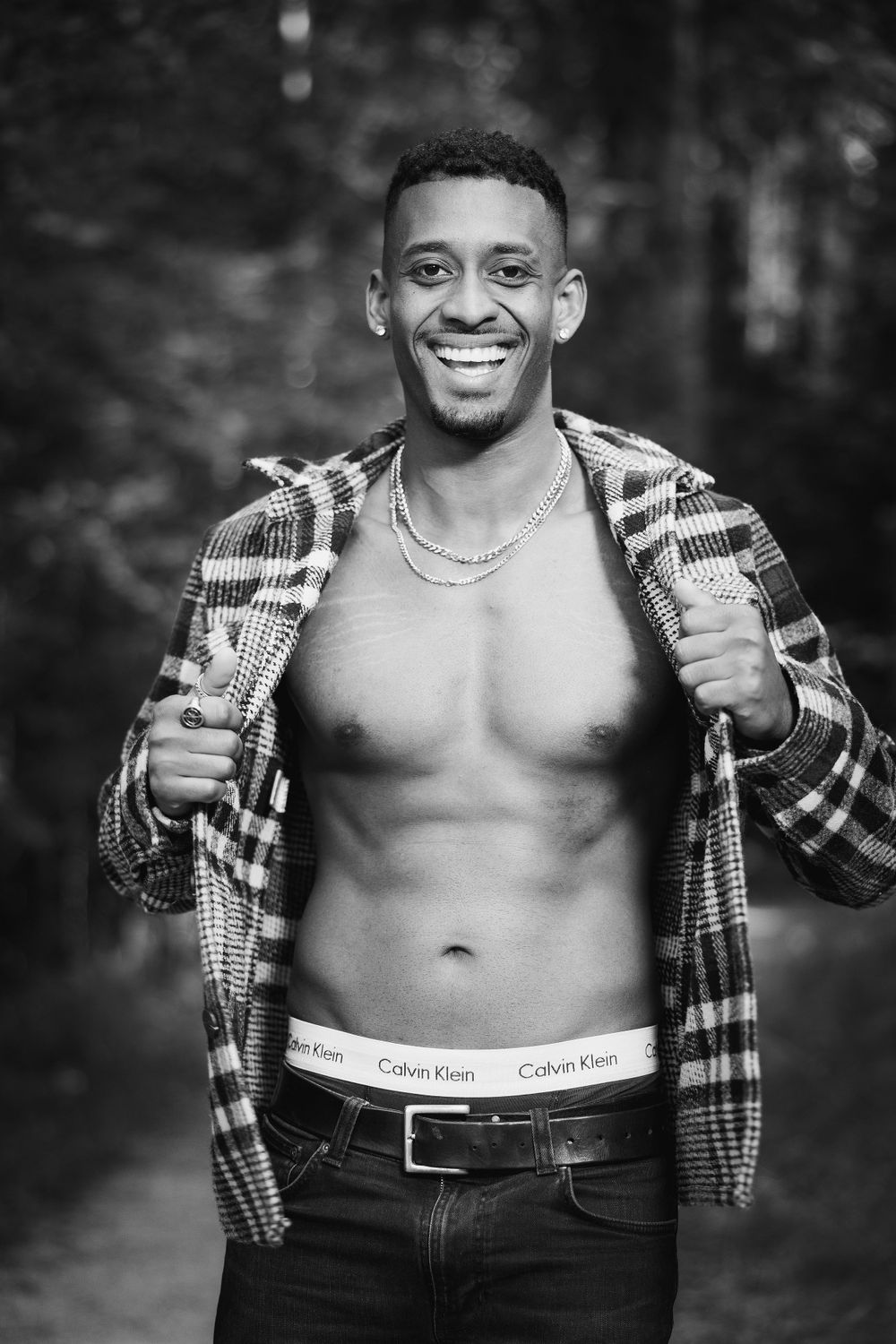 Athletic model in plaid shirt poses confidently in black and white forest portrait.