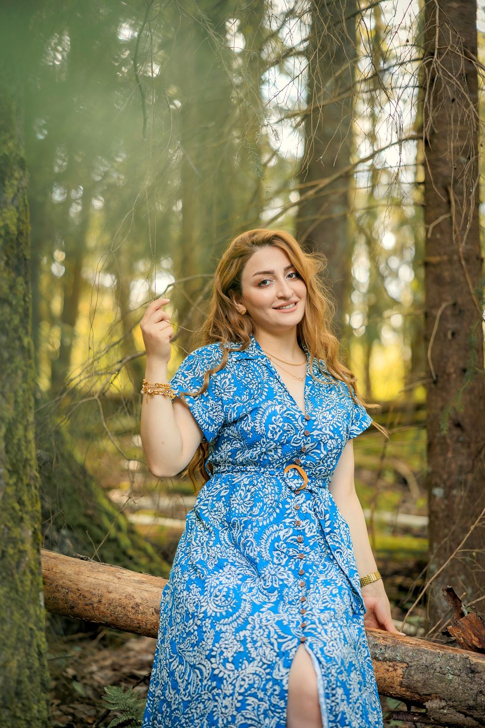 Woman in blue floral dress poses playfully in enchanted forest setting.