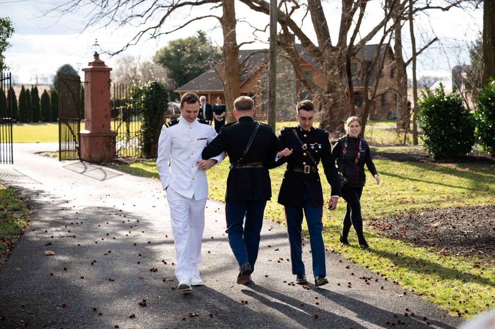 Group walking together on sunny path with white pillars and green landscaping.