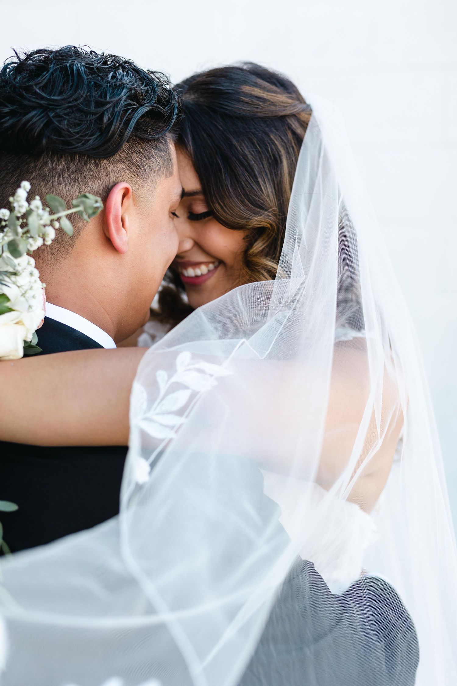 Intimate wedding moment with flowing white veil and delicate flowers.