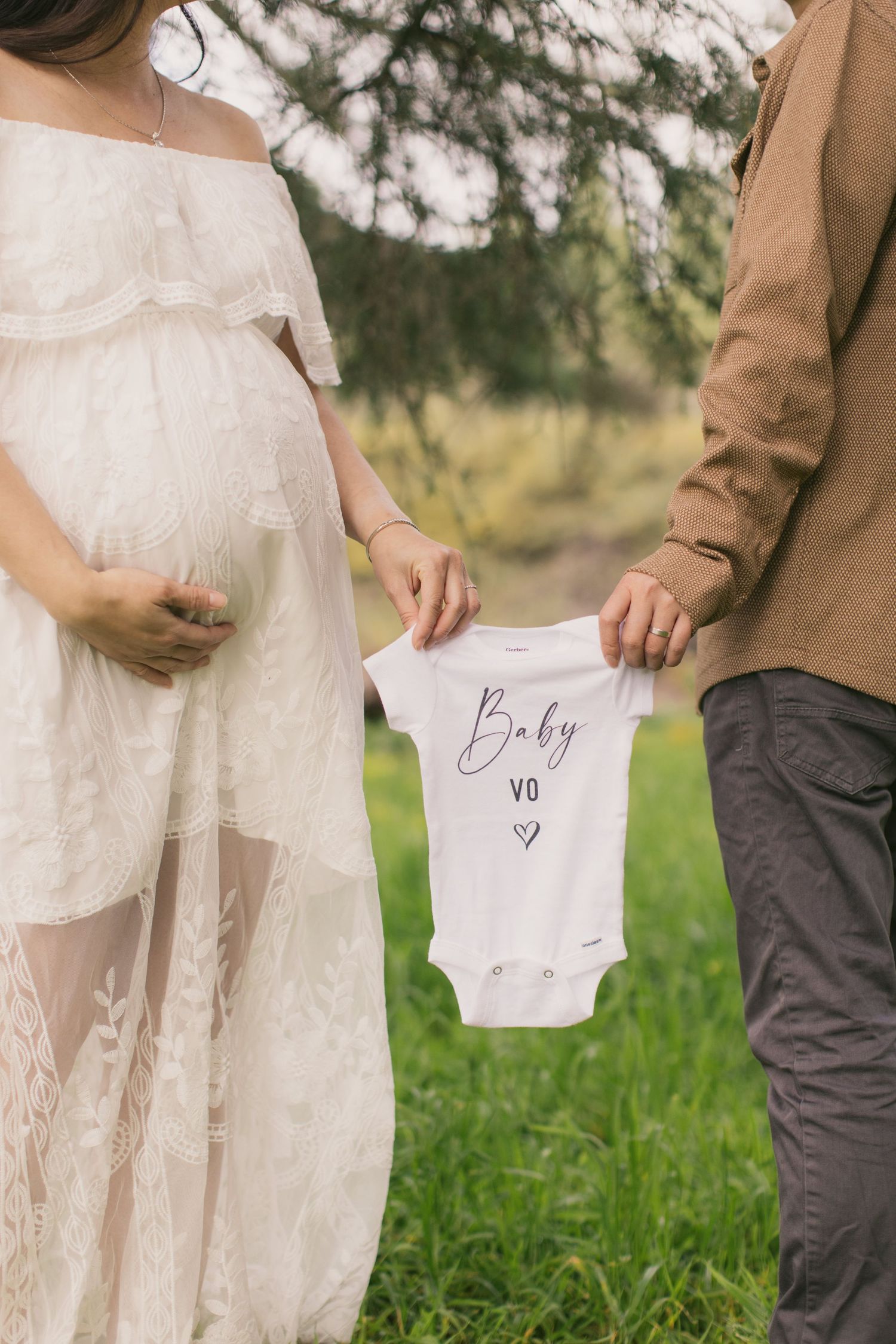 Close-up of couple holding baby onesie during pregnancy announcement photoshoot.