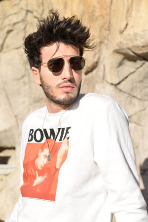 Close-up of white Bowie sweatshirt and aviator sunglasses against stone wall.
